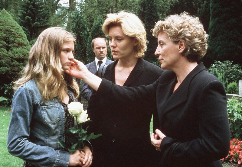 Am Grab ihrer Mutter wird Hannah (Nadine Fano, l.) von der Sekretärin Lilly (Peggy Lukac, r.) und ihrer Tante Nicole (Maike Bollow) getröstet. – Bild: MDR/​Degeto/​Boris Laewen