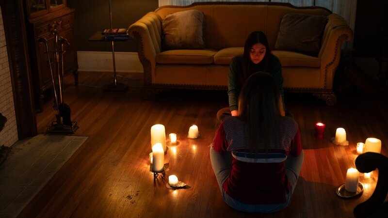RECREATION – Tina Bowen (Christina Giordana Zaros) and Karen Bowen (Olivia Morgan Bell) sit on living room floor surrounded by candles, attempting to contact their deceased mother using a spirit board. – Bild: Warner Bros. Discovery, Inc. or its subsidiaries and affiliates