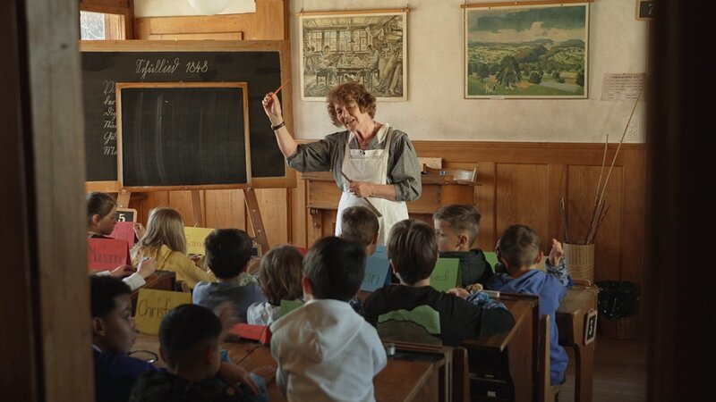 Blick in historisches Klassenzimmer mit Lehrerin und Schüler:innen beim Unterricht – Bild: SRF