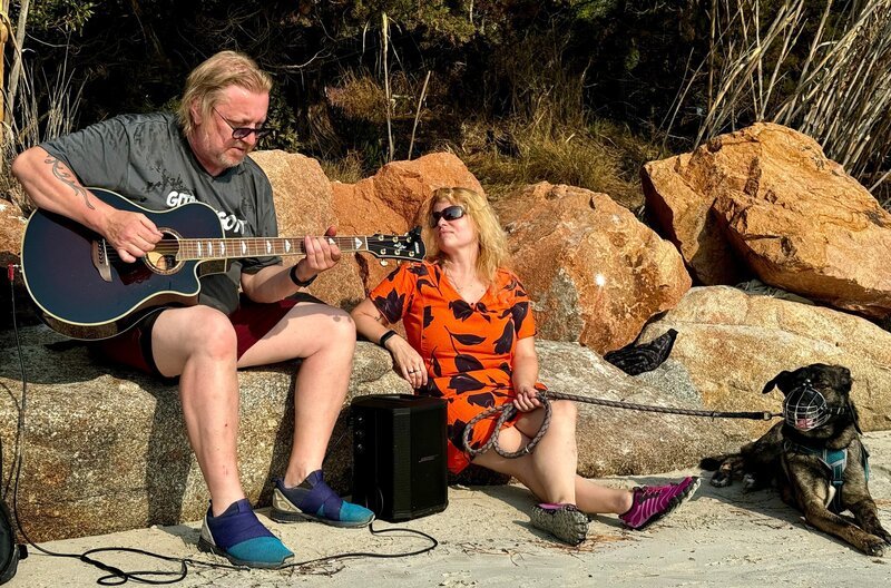 Nicole (r) und Hund Yuri hören sich am Plage Santa Giulia Zappis für die Reise komponierten Song von Andreas an. – Bild: WDR/​Sagamedia Film- Fernsehproduktion GmbH