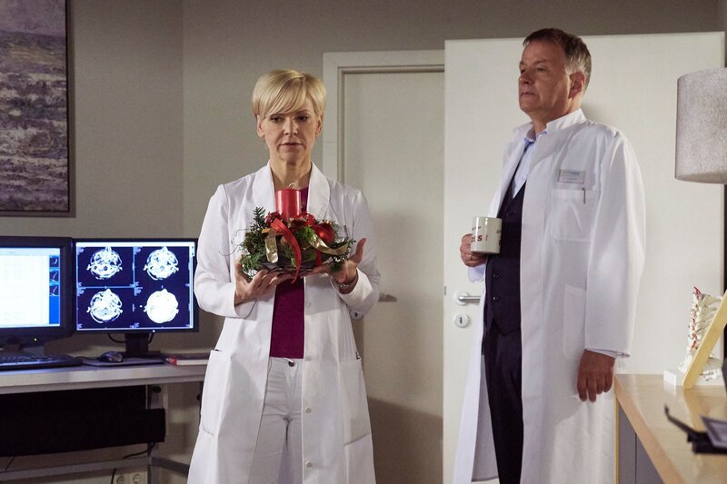 Dr. Kathrin Globisch (Andrea Kathrin Loewig) räumt aus Rücksicht auf seine Allergie, den Weihnachtsschmuck aus Dr. Roland Heilmanns (Thomas Rühmann) Büro. Roland versucht sie scherzhaft des Diebstahles zu bezichtigen – doch beide wissen, dieses Jahr ist alles anders. Es wird das erste Weihnachten ohne Pia Heilmann, Rolands Frau. – Bild: MDR/​Saxonia Media/​Wernicke