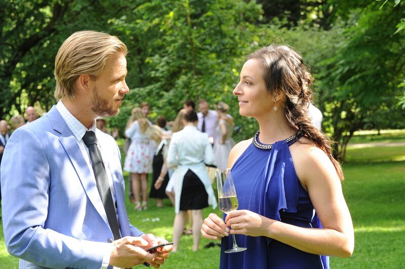 Während die Gäste (Komparsen, Hintergrund) die Verlobung von Julius Weber (Frederic Heidorn, l.) feiern, hat der vor seiner Verlobten ein Geheimnis, von dem Carla Schmitt (Dagny Dewath, r.) weiß. – Bild: ZDF/​MARKUS-FENCHEL