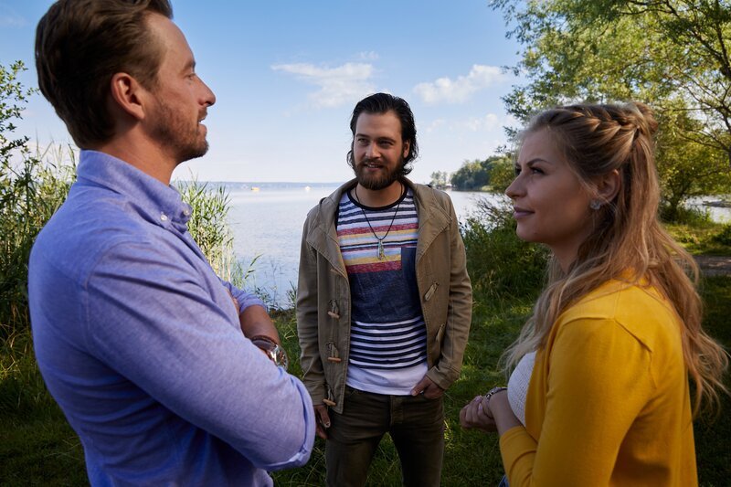 Julian Trautmann (Patrick G. Boll, M.) zeigt Christin Lange (Sarah Thonig, r.) und Andreas Lorenz (Ben Blaskovic, l.) das Grundstück am See, auf dem er seinen Surfbrettverleih eröffnen will. – Bild: ZDF/​Bojan Ritan
