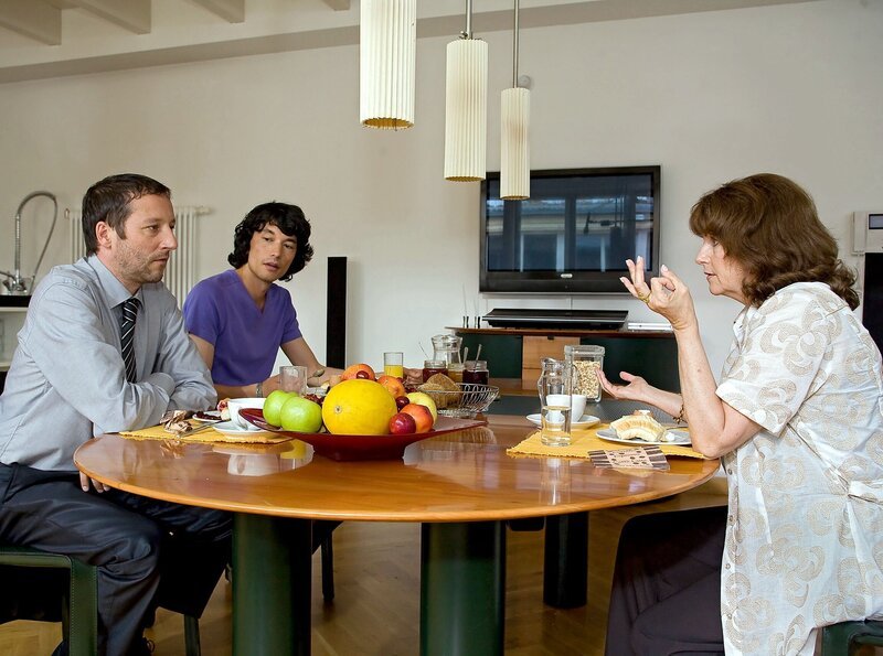 Helene Hummel (Hanna Petkoff, rechts) ist zu Besuch bei ihrem Sohn Alexander (Oliver Broumis, links) und dessen Lebensgefährten Jens Berger (Hyun Wanner). Im Gegensatz zu Alexander, der ein sehr streitbares Verhältnis zu seiner Mutter hat, versteht sich Jens mit ihr tadellos. – Bild: MDR/​MDR/​Saxonia Media/​Krajewsky