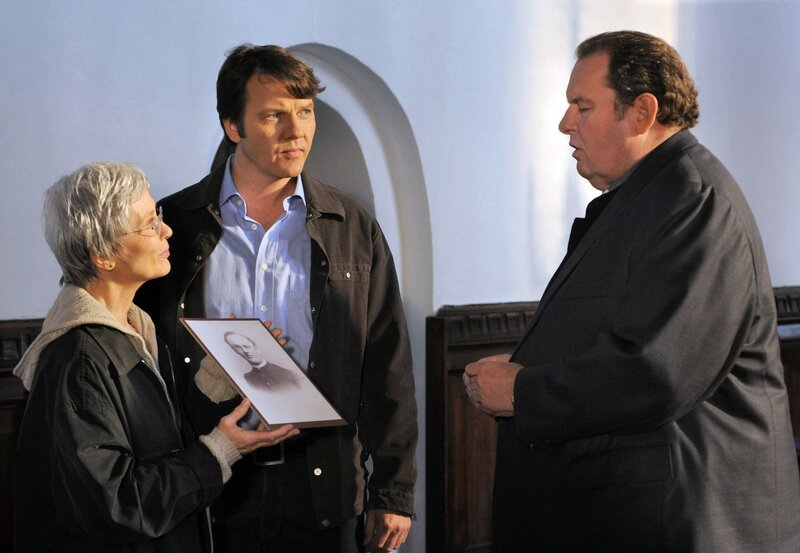 Pfarrer Braun (Ottfried Fischer, rechts) spricht mit seinen Gemeindemitgliedern, der Archivarin Karin Simon (Kornelia Boje) und Holger Gützkow (Christian Rudolf). – Bild: ZDF/​rbb/​Degeto/​Reiner Bajo