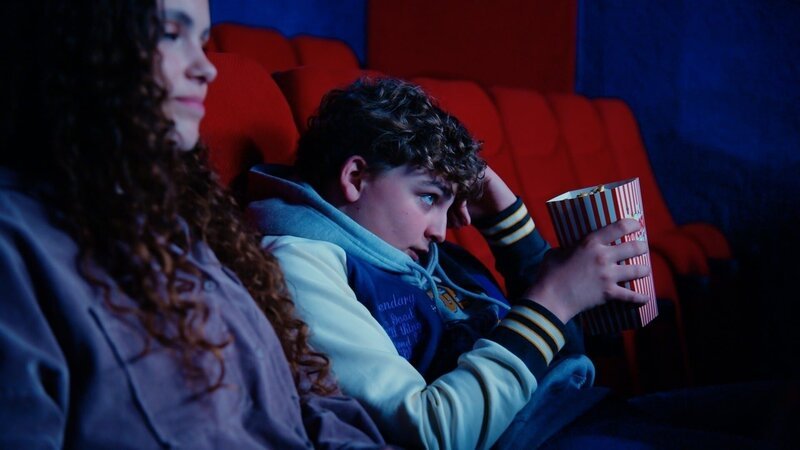 Kaj (Thijs Luijer, rechts) trifft sich mit Romy (Ninthe van Schie) im Kino. Er schämt sich, denn seine Mütter sind ihm gefolgt und benehmen sich einige Reihen weiter hinten daneben. – Bild: ZDF/​Haegens Media