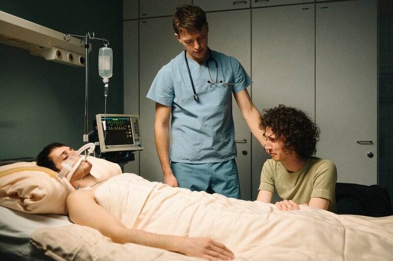 Bernhard Hoestermann (Clemens Bobke, M.) pflegt Heiko (Evangelos Tsarkowistas, l.) während Dirk (Benjamin Viziotis, r.) an seinem Bett sitzt. – Bild: ZDF und ELLIOTT KREYENBERG