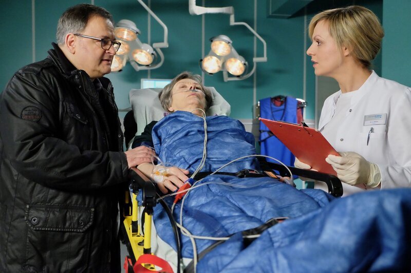 Hans-Peter Brenners (Michael Trischan, links) Mutter Luise (Monika Lennartz, Mitte) ist zusammengebrochen. Während der Untersuchung durch Dr. Lea Peters (Anja Nejarri, rechts) weicht er nicht von ihrer Seite, was Leas Arbeit nicht leichter macht. – Bild: BR/​MDR/​Saxonia Media Filmproduktions GmbH /​ Sebastian Kiss