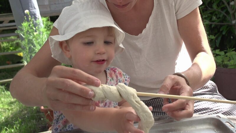 Hedda und Alma backen mit ihren beiden Mamas und ihren beiden Papas Stockbrot. – Bild: WDR/​Die Sendung mit dem Elefanten