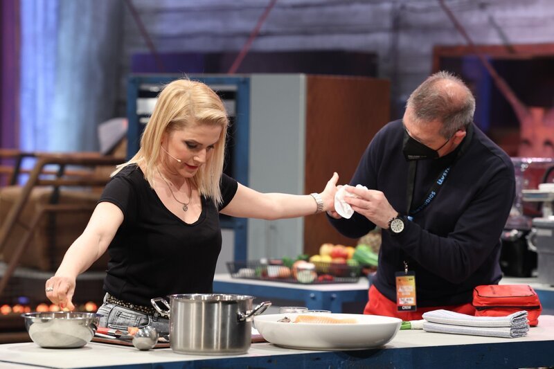 Jeanette Biedermann (l.) hat sich geschnitten. Während sie verarztet wird, kocht sie weiter. – Bild: TVNOW /​ Frank W. Hempel