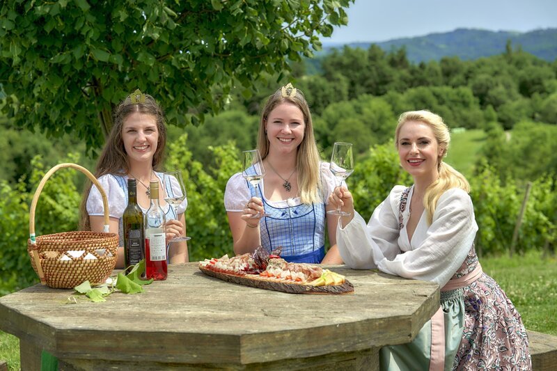 Silvia Schneider mit den Weinhoheiten Marlene Prugmaier und Katrin Strohmaier am Grenztisch. – Bild: ORF/​Silvia Schneider GmbH/​Christian Vogel