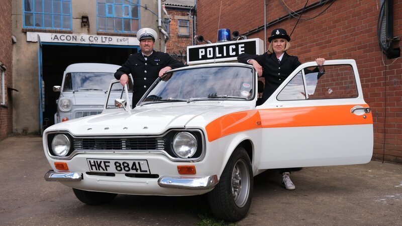Polizeiauto mit posierendem Polizisten (Transit im Hintergrund) – Bild: Discovery, Inc.