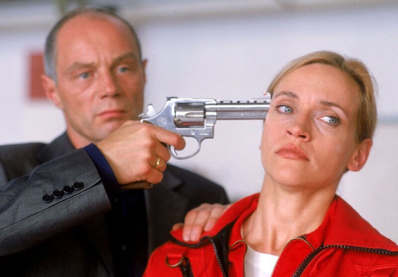 Karin Thaler (Roswitha Meyer) wird von Alex Murnau (Andreas Stoek) mit dem Revolver in Schach gehalten. Der Gangster glaubt, dass das Medicopter-Team im Besitz des Geldes ist und droht sie alle zu töten, wenn er das Geld nicht bekommt. – Bild: RTLplus