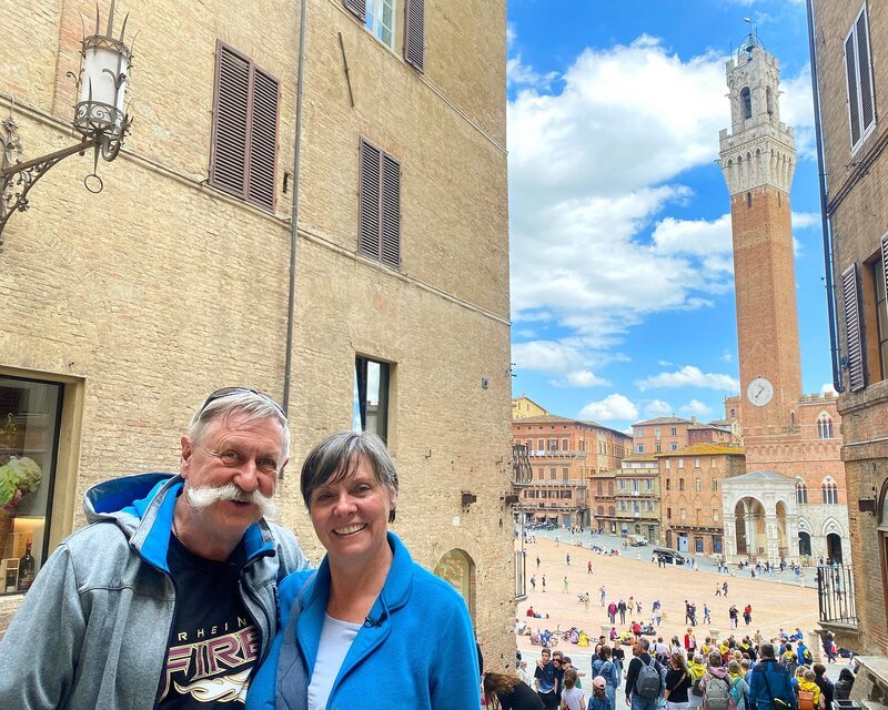 Petra (65) und Rüdiger (66) Erbslöh in den Gassen von Siena mit dem Piazza del Campo und dem Palazzo Pubblico mit dem Torre del Mangia im Hintergrund. – Bild: WDR/​Sagamedia GmbH