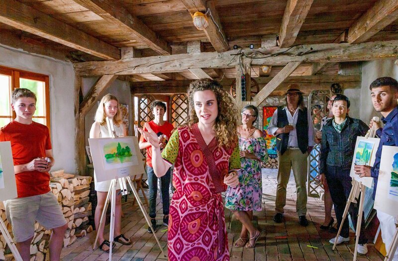 Die Kunstlehrerin Aline Schöttler (Elisabeth Kanettis, M.) eröffnet die Ausstellung „Magisches Morgenlicht“. – Bild: ORF/​Bavaria/​ARD/​SWR/​Daniel Schmid