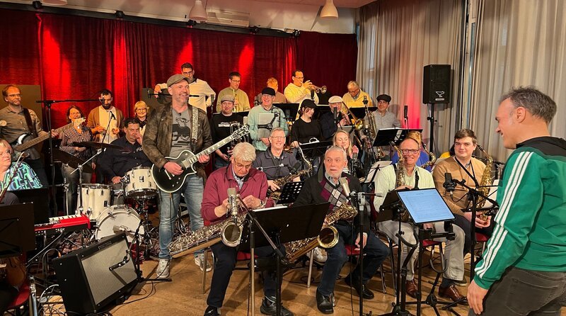 Doc Esser (stehend mit Gitarre) performt mit der Big Band Bergisch Gladbach. Einen Teil der Truppe coacht er in ein gesünderes und fitteres Leben. – Bild: WDR/​solis TV