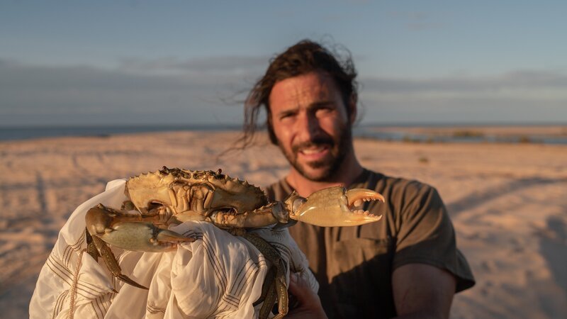 Hazen Audel hält eine lebende Krabbe im australischen Outback. – Bild: Correll Johnson /​ National Geographic