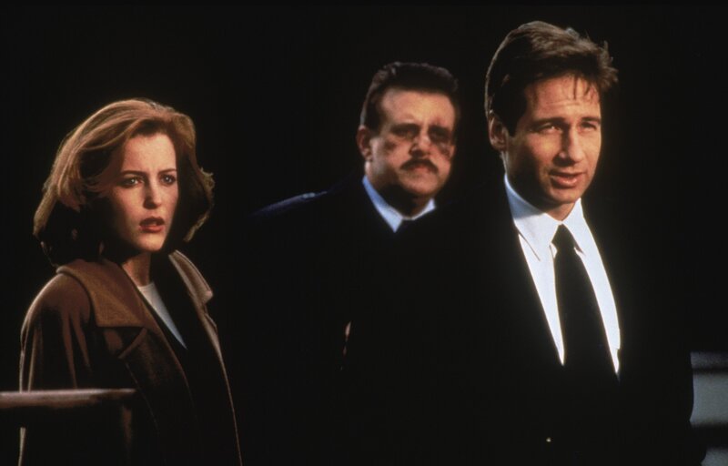Dana Scully (Gillian Anderson, l.); Agent Frank Burst  (Vic Polizos, M.);  Fox Mulder (David Duchovny, r. ) – Bild: 1995⁠–⁠1996 Twentieth Century Fox Film Corporation. All rights reserved. Lizenzbild frei