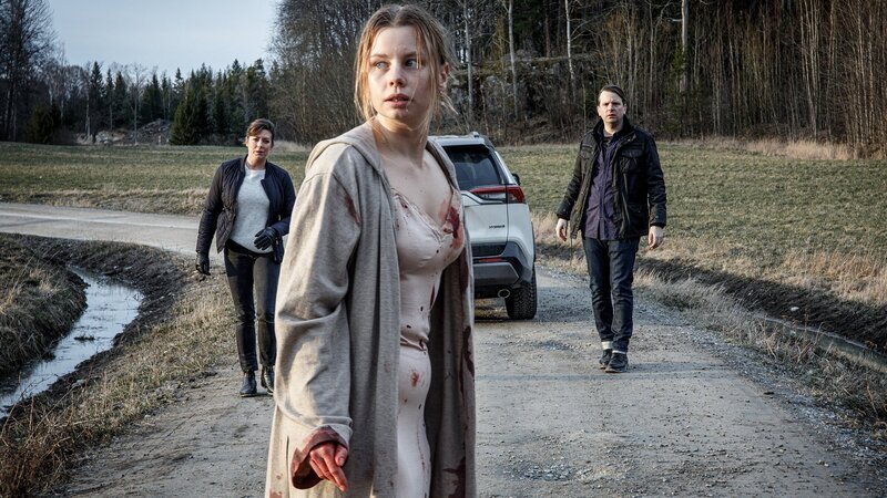 Ida Lind (Amanda Jansson, M.) konnte sich aus ihrer Gefangenschaft befreien und flüchten. Auf einem Feldweg stößt sie auf Alexandra Beijer (Jennie Silfverhjelm, l.) und Oskar Bergman (Måns Nathanaelsson, r.), die versuchen, die verstörte und panische Frau zu beruhigen. – Bild: ZDF und Johan Paulin
