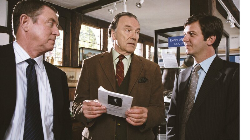Barnaby (John Nettles, l.) und sein Assistent Jones (Jason Hughes, r.) zeigen Heimatmuseumsdirektor Giles Cato (Michael Elwyn, M.) eine Grusel-Broschüre über Spukhäuser in Midsomer. – Bild: ZDF