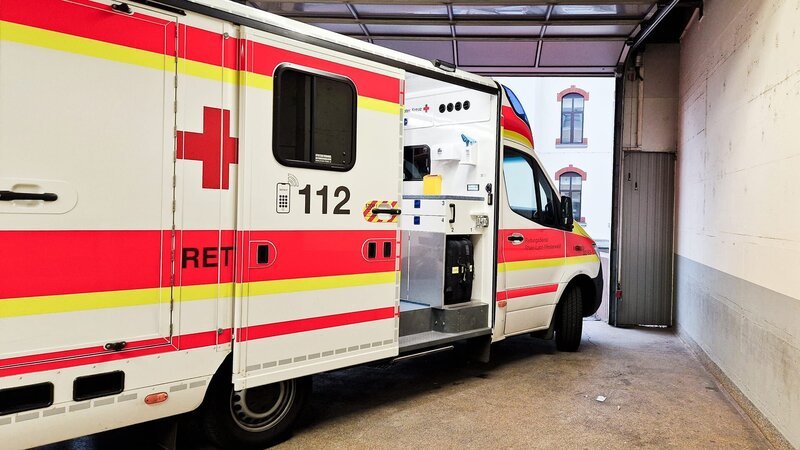 E5 – An ambulance with open sliding door in a garage. It belongs to the German Red Cross. The emergency call number is to be seen. – Bild: Warner Bros. Discovery, Inc. or its subsidiaries and affiliates