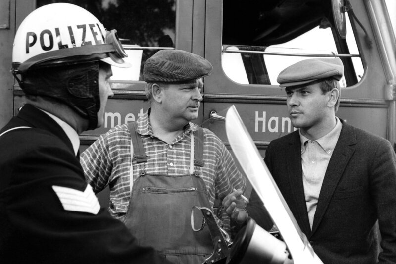 Max Schubert und der Jockey Otto Findler fahren einen Transport zur Rennbahn in Hamburg-Farmsen. Unterwegs bekommen zwei Pferde Kolik. Streifenfahrer Hartmann lotst den Wagen eilig zum Veterinär. Dessen Diagnose lautet: Vergiftung! Der Verdacht fällt auf den Hilfstrainer Lothar Janssen, den Gestütsbesitzer Alberti jüngst entlassen hat. Zwischen den Boxen wird Janssen hinterrücks niedergeschlagen. So legen sich Koldehoff und Hartmann in Stallnähe auf die Lauer, und bald schon haben sie die richtige Spur. Hilfe für seine erkrankten Pferde braucht Jockey Findler (Klaus Löwitsch, rechts). Streifenfahrer Hartmann (Karl-Heinz Heß, links) bietet sich an, den Fahrer des Transportwagens (Ernst Grabbe) zum Tierarzt zu lotsen. – Bild: NDR/​Ambor