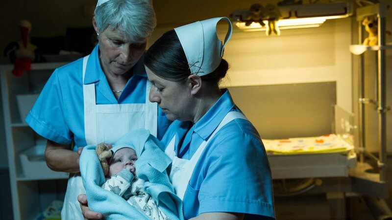 Gemeinsam mit einer Kollegin (Komparsin, l.) kümmert sich Schwester Evi Neumann (Tilla Kratochwil, r.) rührend um ein Neugeborenes (Komparse), das gerade in der Babyklappe abgegeben wurde. – Bild: ZDF