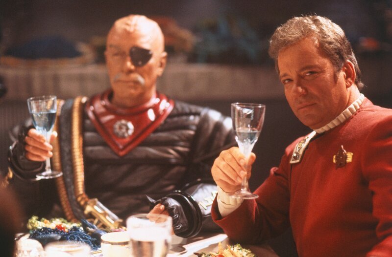 Der festliche Schein trügt: Captain James T. Kirk (William Shatner, re.) ist es gar nicht recht, mit Kanzler Gorkon (David Warner, li.) an einem Tisch sitzen zu müssen. – Bild: Paramount Pictures