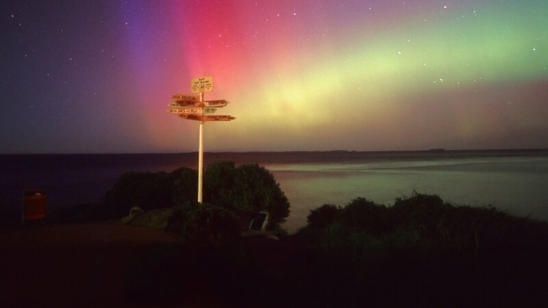 Dieses Bild zeigt den berühmten leuchtend gelben Wegweiser am Stirling Point in Bluff, Neuseeland, vor dem Hintergrund eines beeindruckenden Schauspiels der Aurora Australis (Südlichter). – Bild: Curiosity TV