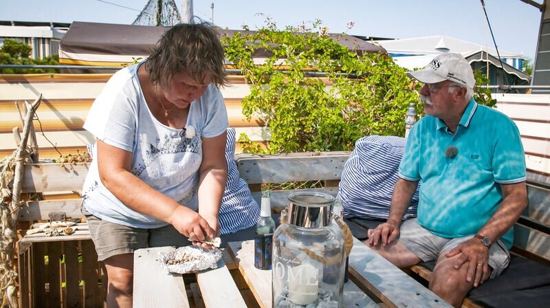 Deko für die Camping-Lounge. Peter und Heike haben sich aus Holzpaletten eine pfiffige Sitzgelegenheit gebaut – im Vintagestil. Damit die richtig wirkt, muss jetzt aber noch typische Nordsee Deko her: Die beiden Dauercamper machen sich deshalb auf Muschelsuche. – Bild: MDR/​timeline