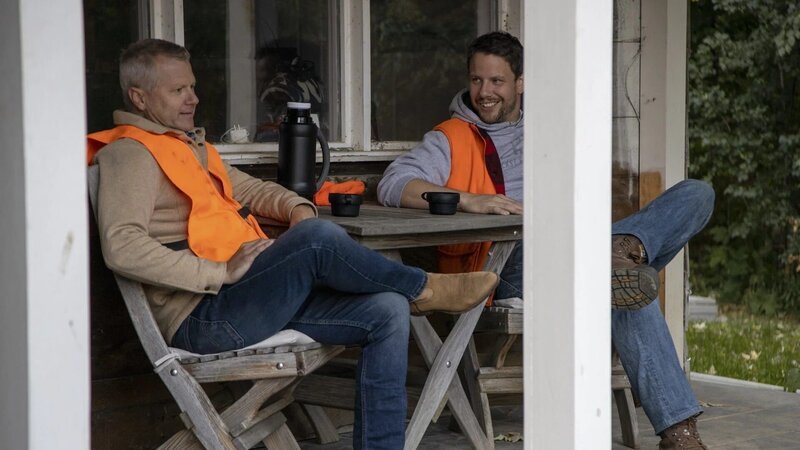 Zwei Männer sitzen auf der Terrasse vor dem Haus. – Bild: The Movie Database (TMDb)
