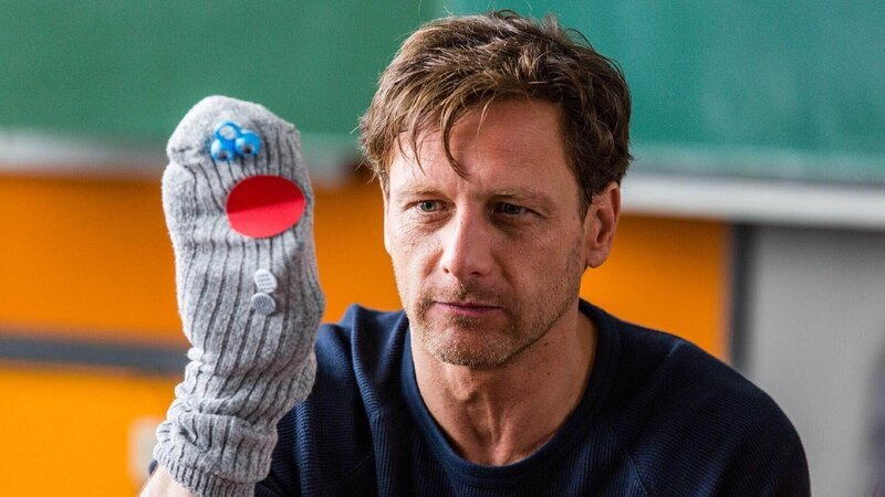 Stefan Vollmer (Hendrik Duryn) lockert seinen Deutschunterricht für die Flüchtlinge mit einer Handpuppe auf – seine Schülerin Anne ist von so viel Engagement begeistert … – Bild: TVNOW /​ Frank Dicks /​ Sony Pictures FFP