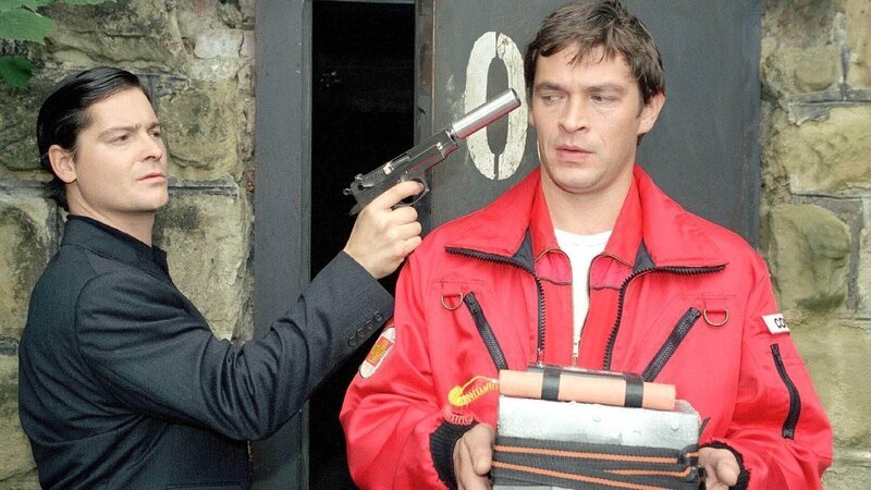 Enrico Contini (Tom Mikulla, r.) erklärt sich bereit, die Übergabe Plutonium gegen Diamanten durchzuführen. Er wird von Wörz (Fritz Karl), dem Erpresser, mit der Waffe bedroht. – Bild: MG RTL D /​ Miguel Dieterich