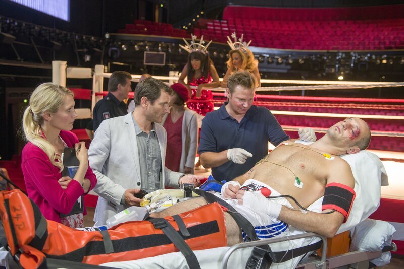 Drew Sarich (Drew Sarich, r.) der Hauptdarsteller des Musicals „Rocky“ ist nach einer Vorstellung hinter der Bühne zusammengebrochen. Haase (Fabian Harloff, 2.v.r.) kümmert sich um seinen Patienten und lässt den künstlerischen Leiter Mikkelsen (Alex Brendemühl, 2.v.l.) und dessen Assistentin Janne (Mareile Moeller) gleich wissen, dass sie mit Drew für die Abendvorstellung nicht mehr rechnen können. – Bild: ZDF/​Boris Laewen