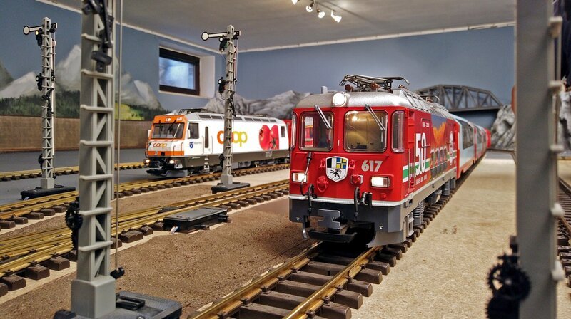 Zwei LGB-Modelllokomotiven bei der Rhätischen Bahn in der Schweiz: vorne eine Ge 4/​4 II mit Sonderbedruckung ‚50 Jahre LGB‘, links eine Ge 4/​4 III mit Coop-Werbung. – Bild: SWR