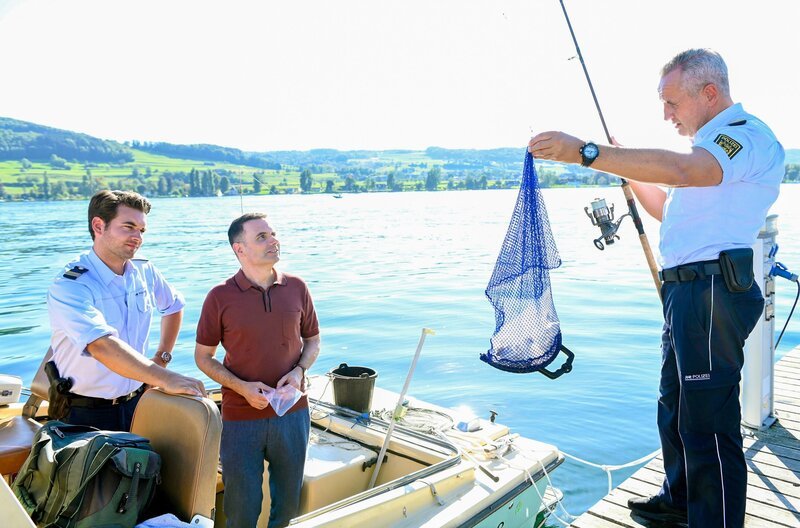 Jakob Frings (Max König, li.) wartet gespannt auf die Erklärung des Schmuckhändlers Florian Arlen (Carsten Strauch, M.) zu dem Fund, den sein Kollege Paul Schott (Tim Wilde, r.) soeben aus dem Wasser gefischt hat. – Bild: ORF/​Bavaria/​ARD/​SWR/​Laurent Trümper