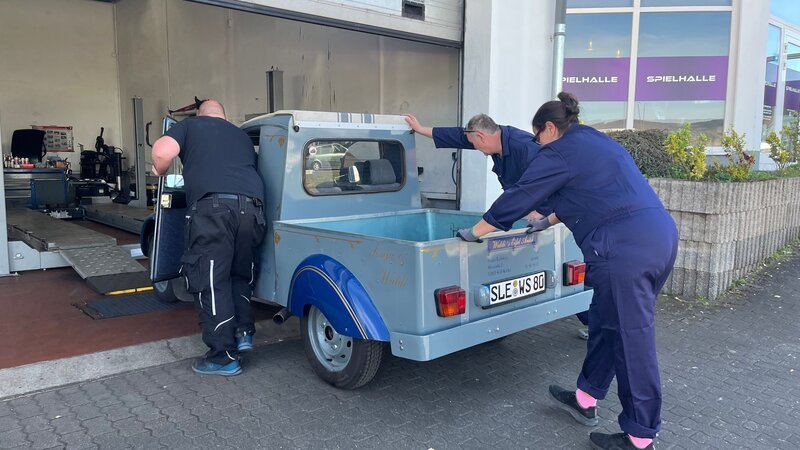 Waldi (M.) und Sonja (r.) schieben ihre Ente mit einem Helfer (l.) in die Werkstatt. – Bild: ZDF und Warner Bros. Deutschland