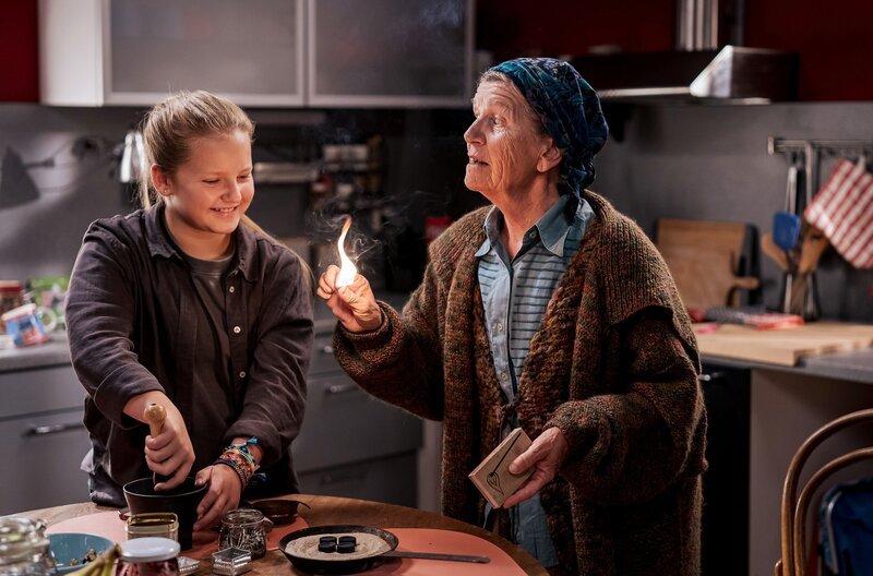 Lioba (Lisbeth Felder, re.) zeigt der „Junghexe“ Carlotta (Mila Breiter) ein Ritual, das helfen soll, die schlechten Energien zu vertreiben. – Bild: SWR/​Christian Koch