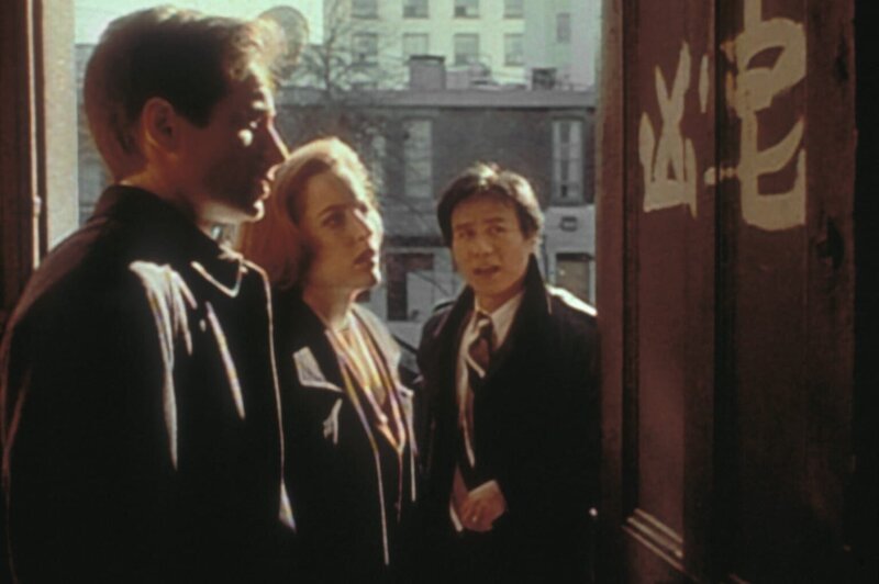 Obwohl Detective Glen Chao (B.D. Wong, r.) chinesischer Abstammung ist, kann er die Schriftzeichen an der Wohnungstür eines Mordopfers für Mulder (David Duchovny, l.) und Scully (Gillian Anderson, M.) nicht übersetzen. – Bild: TM + © 2000 Twentieth Century Fox Film Corporation. All Rights Reserved. Lizenzbild frei
