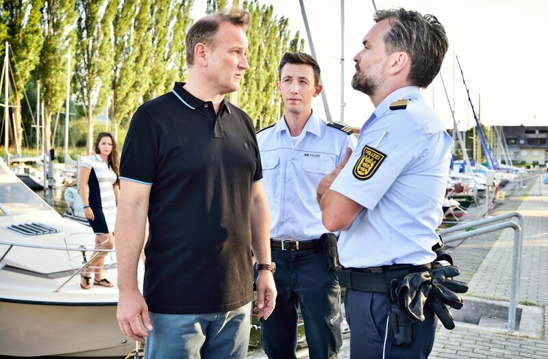 Pirmin Spitznagel (Simon Werdelis, M.) und Andreas Rambach (Ole Puppe, r.) setzen Andreas Holler (Thomas Douglas, l.), den Vorsitzenden des Segelclubs, unter Druck. – Bild: ORF/​Bavaria/​ARD/​SWR/​Patrick Pfeiffer