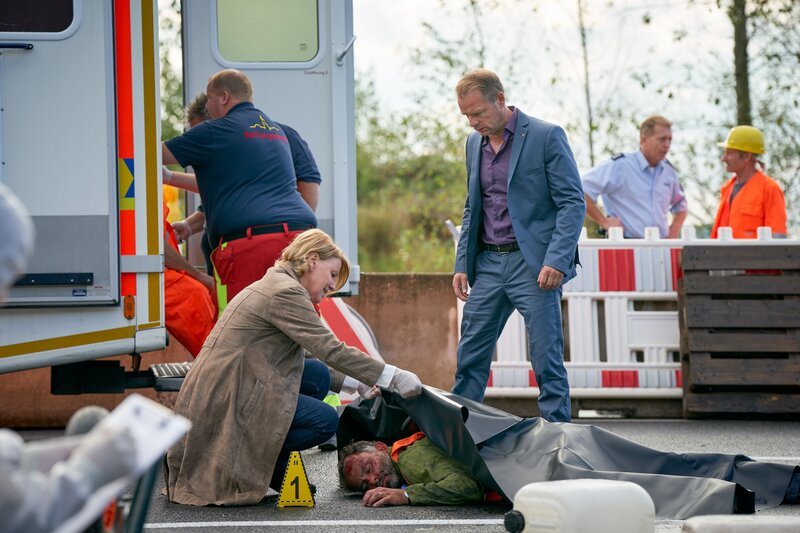 Marie Brand (Mariele Millowitsch, l.) zeigt ihrem Kollegen Jürgen Simmel (Hinnerk Schönemann, r.) die Leiche von Claudio Messina (Sami Loris, M.) und sie untersuchen den Tatort. – Bild: Guido Engels /​ ZDF