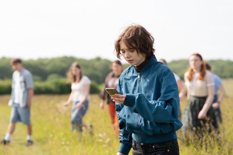 Pip Fitz-Amobi (Emma Myers, v.) koordiniert die Suche nach Jamie per Handy, während im Hintergrund Mitschüler das Feld durchkämmen. Die Zeit drängt. – Bild: ZDF und Ikram Ahmed