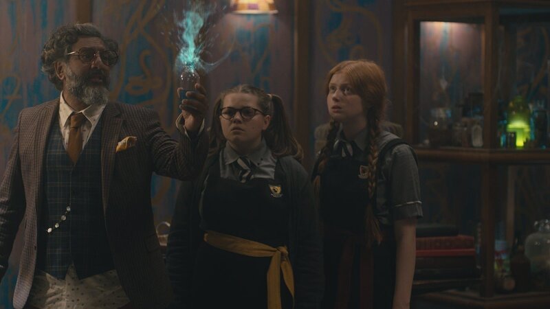 Maude (Megan Hughes, M.) hat es geschafft, Mildred (Lydia Page, r.) wieder auf die Grausteinakademie zurückzuholen. Mit Herrn Ginsengs (Nitin Ganatra) Hilfe wollen sie aus Mildreds Reparier-Zaubertrank einen Aufhebungszaubertrank herstellen, um damit Frau Graustein aus den Scherben wiederherzustellen. – Bild: CBBC/​ZDF Enterprises /​ ZDF