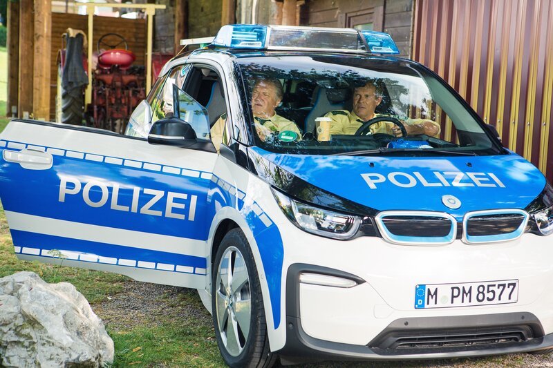 Hubert (Christian Tramitz, r.) und Girwidz (Michael Brandner, l.) warten im neuen, elektrischen Streifenwagen auf Riedls Meldung. – Bild: TMG /​ Kai Neunert