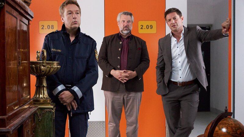 Polizeihauptmeister Mohr (Max Müller, l.) führt die Kommissare Stadler (Dieter Fischer, M.) und Hansen (Igor Jefti?, r.) zu dem vom Mordopfer angemieteten Lagerraum. Ob die dort aufbewahrten Antiquitäten aus der Wohnung des Opfers stammen? – Bild: ZDF