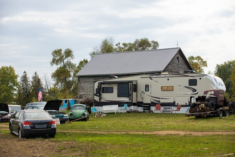 Ein Hof mit einem Wohnwagen, alten Automobilen und einer Holzscheune. – Bild: zlwFmental /​ DCL /​ Scott Brothers Entertainment