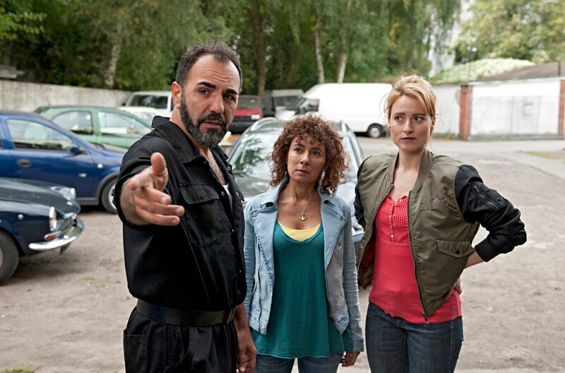Für Werkstattbesitzer Can Topal (Adnan Maral, l.) erklärt Nina Sieveking (Wanda Perdelwitz, r.) und Harry Möller (Maria Ketikidou, M.), dass nur die Jugendbande Lions für den Diebstahl seines Oldtimers in Frage kommt. – Bild: ARD/​Thorsten Jander