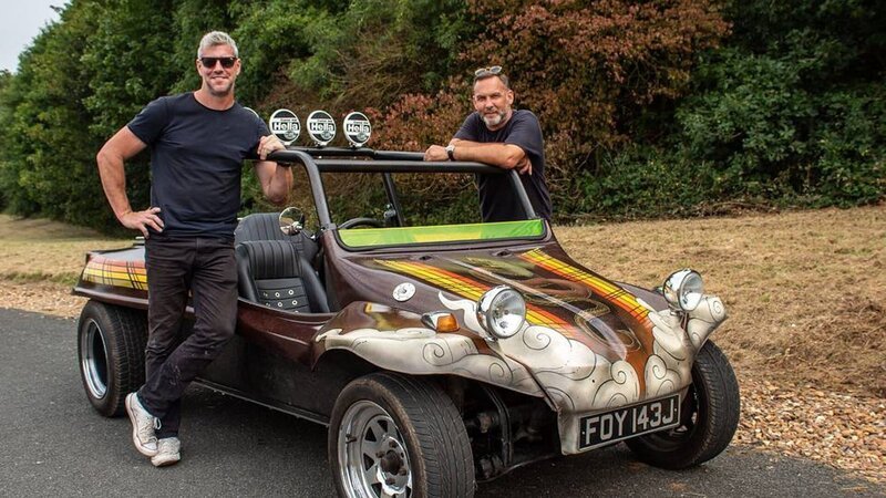 ANT ANSTEAD, wearing sunglasses, black T-shirt and jeans, leaning on the roll bar of the VW Buggy, with Duncan Cowper standing on the other side of the buggy, shot at Millbrook Proving Ground, trees in the background, after restoration, side view. – Bild: Warner Bros. Discovery