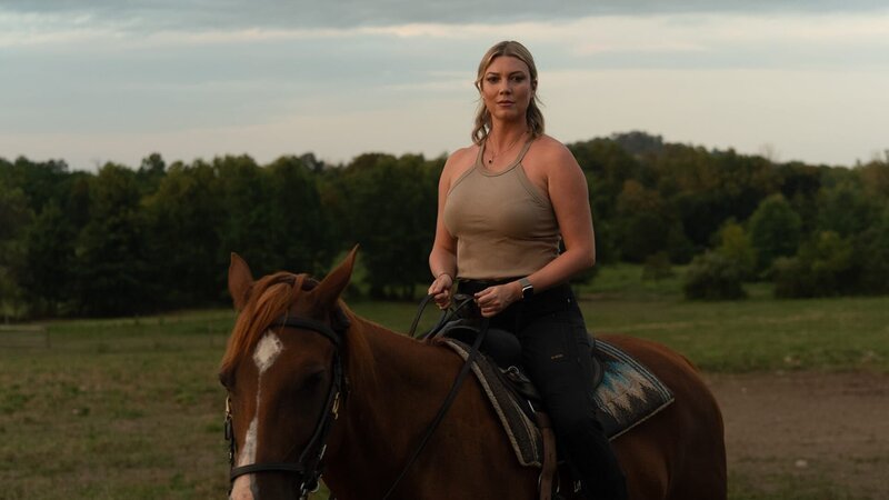Heather A. rides a horse through farmland to her next destination, the southern battlefield. – Bild: Warner Bros. Discovery