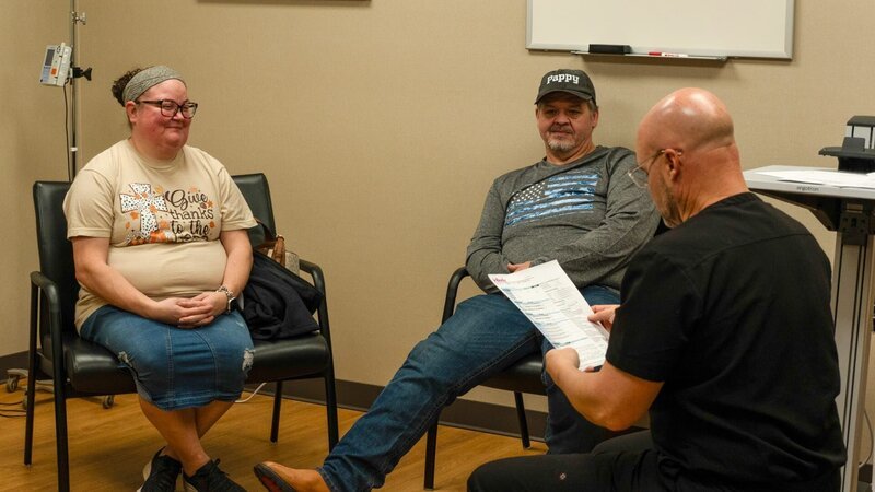 Brittany Combs smiling at surgery approval appointment while Chris Combs looks at Dr. Procter reviewing medical documents. – Bild: Warner Bros. Discovery, Inc. or its subsidiaries and affiliates